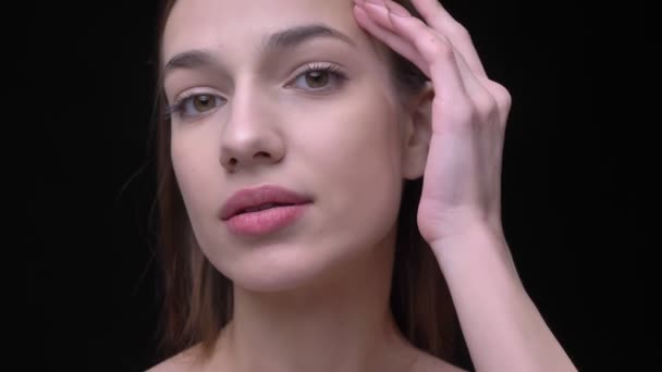 Close-up portret van de jonge Kaukasische meisje met naakt make-up teder het aanraken van haar gezicht op zwarte achtergrond. — Stockvideo