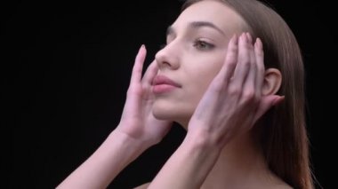 Profil sahibi genç ve ince beyaz kız yavaşça yüzünü dokunaklı ve gözleri siyah arka plan üzerinde kapanış çıplak makyaj ile portre.