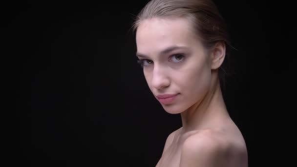 Porträtt i profil av smal kaukasiska tjej med naken make-up långsamt flytta och titta in i kameran på svart bakgrund. — Stockvideo