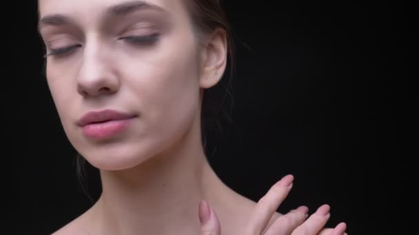 Close-up circling around portrait of slim caucasian girl touching gently her face and watching into camera on black background. — Stock Video