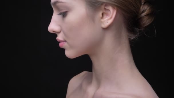 Close-up portrait in profile of slim caucasian girl watching calmly into camera on black background. — Stock Video