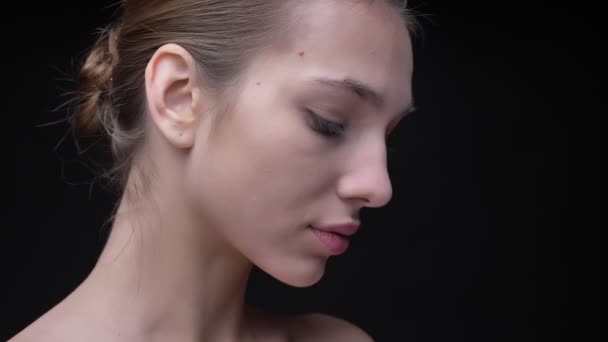 Портрет молодой и худой белой девушки с обнажённым макияжем, медленно движущейся и спокойно смотрящей в камеру на черном фоне . — стоковое видео