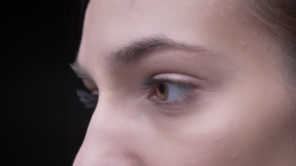 Close-up eye-portrait de menina caucasiana jovem com nude make-up calmamente em movimento e assistindo em câmera no fundo preto . — Vídeo de Stock