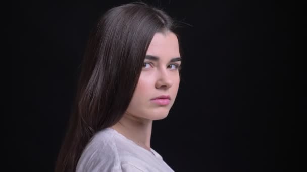 Portrait of young overweight brunette caucasian girl turns to camera and watches seriously into camera on black background. — Stock Video
