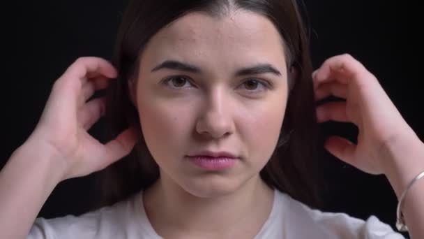 Close-up portrait of young overweight brunette caucasian girl watching seriously into camera on black background. — Stock Video