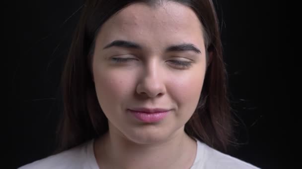 Close-up portrait of young overweight brunette caucasian girl watching smilingly into camera on black background. — Stock Video