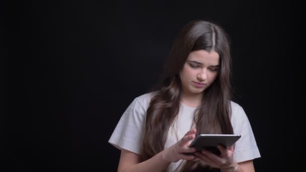 Portrait de jeune fille caucasienne brune en surpoids travaillant attentivement avec une tablette sur fond noir . — Video