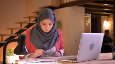 Genç özenli Müslüman işkadını laptop kapalı işyeri önünde grafikteki veri okuyan hijab içinde closeup portresi