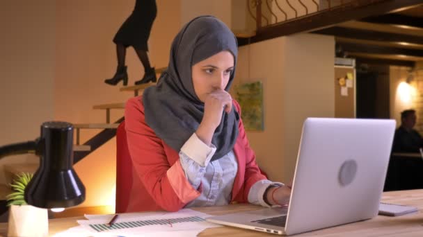 Closeup portret van jonge drukke moslim kantoorbediende in hijab onderzoeken van de gegevens op de diagrammen en grafieken voor de laptop binnenshuis op de werkplek — Stockvideo