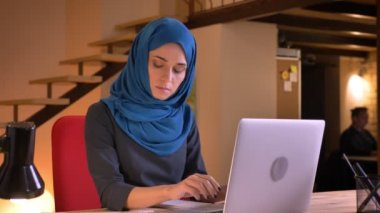 Genç ciddi Müslüman işkadını hijab meşgul ve işyeri üzerinde kapalı acele laptop yazma olmak içinde closeup portresi