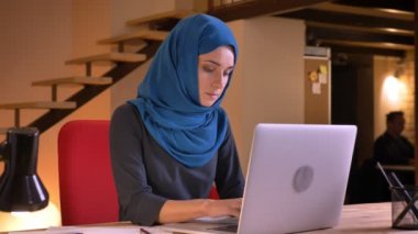 Dizüstü bilgisayarda yazarak sonra kameraya dönüm ve gülümseyen hijab işçisi genç çekici Müslüman kadın ofis portre portre