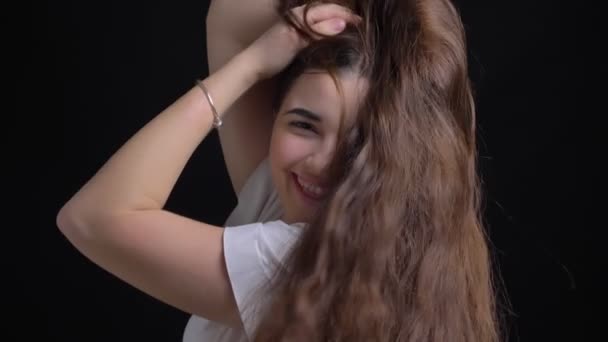 Portrait of young overweight brunette caucasian girl shaking her long hair and joyfully posing into camera on black background. — Stock Video