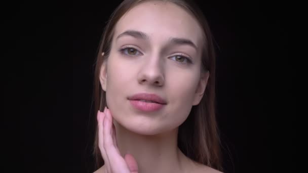 Ung och smal kaukasiska tjej med naken make-up titta in i kameran och röra vid hennes ansikte med tillfredsställelse på svart bakgrund. — Stockvideo