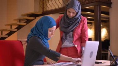 İki genç Arap kadın Ofis çalışanları verileri grafik üzerinde tartışırken hijabs içinde closeup portresi. Genç çalışan iş dostum için bir öneri sorar.