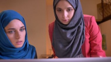 İki genç Arap kadın çalışanların dizüstü bilgisayar kapalı üzerinde çalışma alanı'nı kullanarak konu üzerinde savunarak closeup portresi