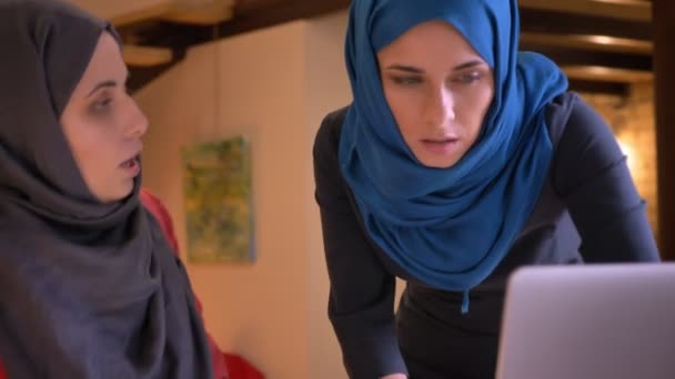 Gros plan de deux jeunes ouvrières arabes de bureau dans les hijabs discutant des données sur le graphique — Video