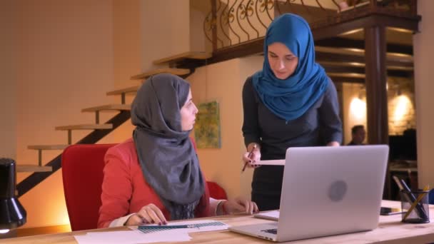 Πορτραίτο closeup νεαρός μουσουλμανική γυναίκα υπάλληλος και εργοδότης συζητώντας τα δεδομένα στο γράφημα μπροστά από το φορητό υπολογιστή. Αφεντικό, επισημαίνοντας σχετικά με τα λάθη που βρέθηκαν στο έργο των νεότερων εργαζόμενος γραφείου — Αρχείο Βίντεο