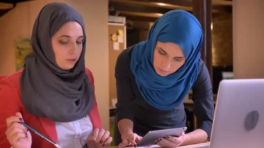 Belgili tanımlık laptop önünde iş konuyu tartışıyor iki genç Müslüman iş kadınları closeup portresi. Onun projede hata yapmak çıktı yeni ofis çalışanı rehberlik işveren
