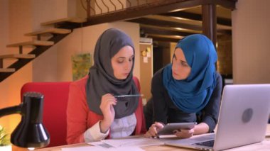 İki genç Müslüman Ofis çalışanları üzerinde bilgi respresented dizüstü bilgisayar kapalı kullanarak grafik üzerinde savunarak hijabs içinde closeup portresi