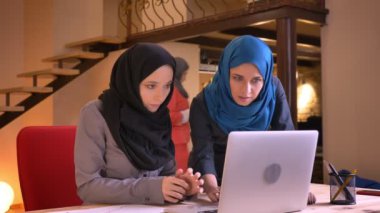 İki genç Müslüman kadın Ofis çalışanları içinde belgili tanımlık laptop önünde ofiste hijabs closeup portresi. İki Arap iş kadınları çalışması