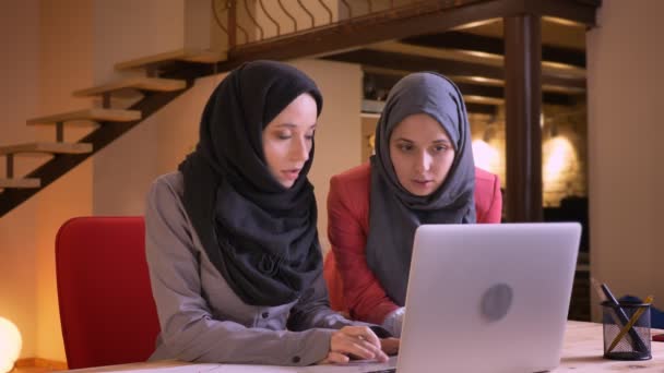 Портрет крупным планом двух молодых мусульманских офисных работниц, использующих ноутбук и предлагающих наилучшее решение проблемы. Командная работа двух арабских бизнесвумен — стоковое видео