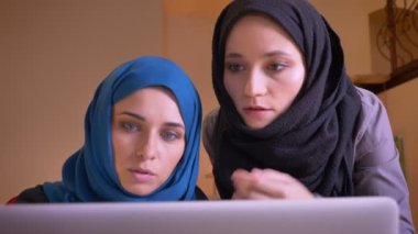 Laptop hakkında bilgi söz hijabs içinde iki genç Müslüman iş kadınları closeup portresi. Bir kadın işçiye talimat patron.