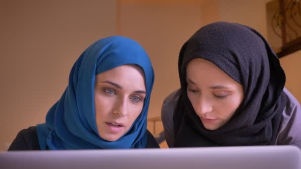 Retrato de close-up de jovens belas mulheres de negócios muçulmanas discutindo um tema de trabalho usando o laptop dentro de casa no local de trabalho — Vídeo de Stock