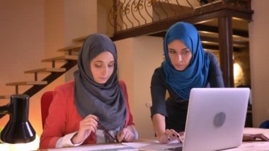 Savunarak ve belgili tanımlık laptop önünde tartışmaya sonra kameraya bakarak ve gülümseyen iki genç Müslüman iş kadınları closeup portresi
