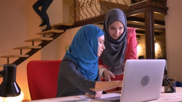 Closeup portret van twee jonge mooie moslim zakenvrouwen emotioneel bespreking van een onderwerp voor de laptop en vervolgens kijken naar camera en glimlachen — Stockvideo