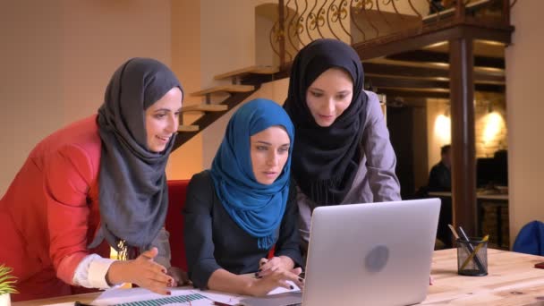 Close-up opnamen van drie vriendelijke moslim vrouwelijke kantoorpersoneel controleren op de laptop en krijgen blij en opgewonden binnenshuis op de werkplek — Stockvideo