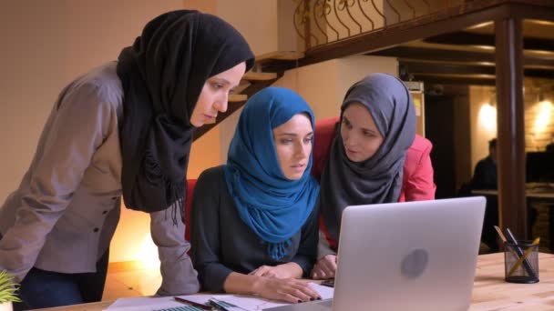 Retrato de close-up de três alegres trabalhadoras de escritório árabes nos hijabs discutindo os dados no laptop com emoção — Vídeo de Stock