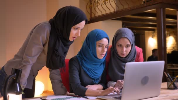 Primo piano ripresa di tre dipendenti musulmani in uscita di sesso femminile avendo una discussione utilizzando il computer portatile poi guardando la fotocamera e sorridendo — Video Stock