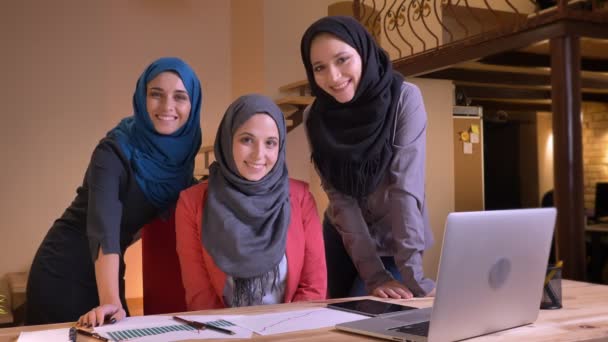 Detailní portrét tří mladých muslimských žen úřad pracovníků ve hijabs přímo do kamery a šťastně se usmívala na pracoviště uvnitř — Stock video
