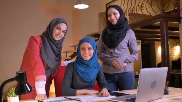 Retrato de cerca de tres hermosas trabajadoras de oficina árabes exitosas mirando a la cámara y sonriendo alegremente en el lugar de trabajo en el interior — Vídeo de stock