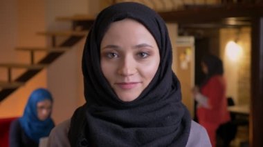 Genç güzel Arap işkadını kameraya bakarak ve mutlu bir şekilde gülerek işyeri kapalı siyah Tesettür içinde closeup portresi