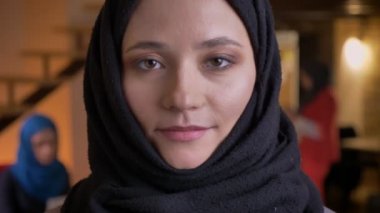 Genç güzel Müslüman kadın ofis çalışanı arka hijab doğruca kameraya tarafsız yüz ifadesi ile seyir içinde closeup portresi