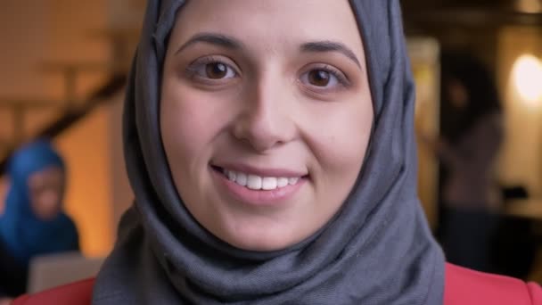 Retrato de close-up de jovem bonito rosto feminino árabe em hijab cinza olhando diretamente para a câmera com olhos muito castanhos e expressão facial sorridente — Vídeo de Stock