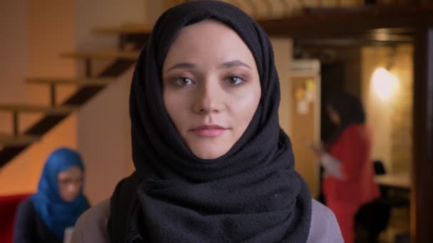 Portrait rapproché d'une jeune femme arabe de bureau en hijab noir regardant directement la caméra et souriant en toute confiance sur le lieu de travail — Video