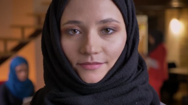 Gros plan portrait de jeune belle musulmane employée de bureau dans le dos hijab regardant directement la caméra avec une expression faciale neutre — Video