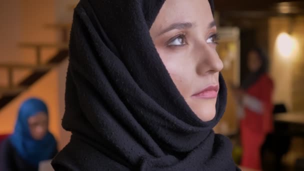 Retrato de cerca de la joven mujer de negocios árabe hermosa en hijab negro girando a la cámara desde el lado y mirando recto — Vídeos de Stock