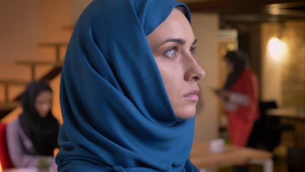 Крупный план портрета молодой красивой мусульманки в синем хиджабе, поворачивающейся со стороны и смотрящей прямо в камеру — стоковое видео