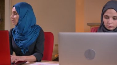Closeup ateş, üç genç başarılı Müslüman mecaz hijabs dizüstü bilgisayarlarda çalışma içinde. İki tane dizüstü bilgisayarda bir veri tartışıyor