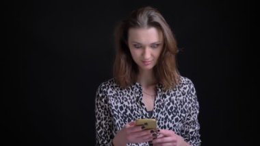 Genç Beyaz esmer kadın kaydırma aşağı telefonda çarpıcı sonra kameraya bakarak ve mutlu bir şekilde gülerek portre portre.