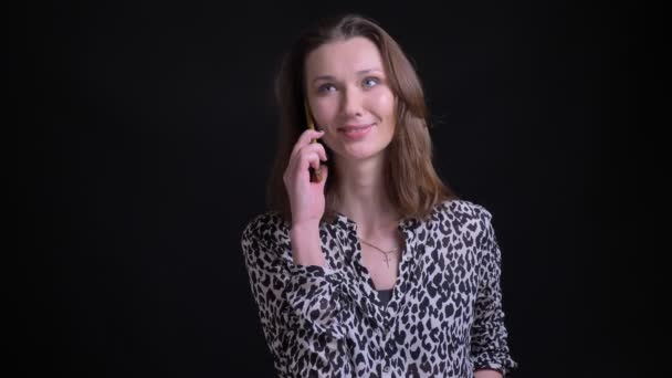 Closeup portret van jonge mooie Kaukasische vrouw een ongedwongen gesprek op de telefoon voor de camera met geïsoleerd op zwarte achtergrond — Stockvideo