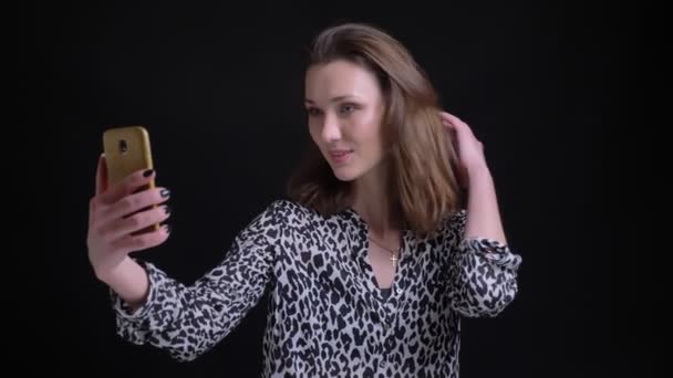 Closeup portrait of young pretty caucasian female taking selfies on the phone smiling and playing with her hair in front of the camera — Stock Video