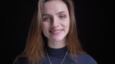 Yakın çekim kamera siyah arka plan üzerine içine sevinçle gülümseyen genç ve ince esmer beyaz kız portresi.