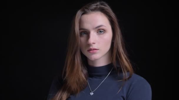 Close-up portrait of young and slim brunette caucasian girl fashionably and seriously posing into camera on black background. — Stock Video