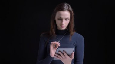 Genç ve dikkatle tablet izliyor ve onun ip kamera için siyah arka plan üzerinde gösterilen ince esmer beyaz kız.