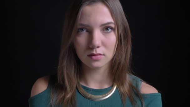 Close-up retrato de jovem morena caucasiana menina assistindo a sério na câmera no fundo preto . — Vídeo de Stock