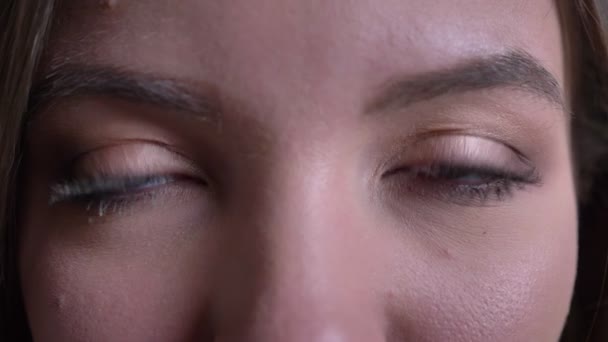 Close-up eye-portrait of young brunette caucasian girl watching calmly into camera on black background. — Stock Video